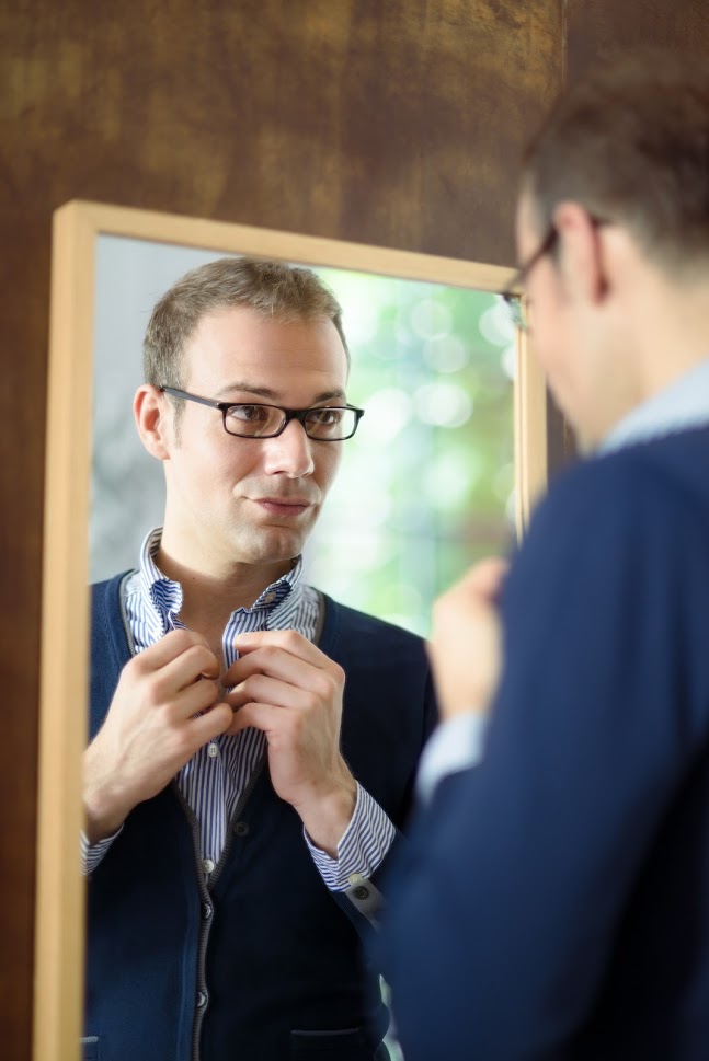 Portrait of young man with glasses getting ready, dressing up and looking at mirror